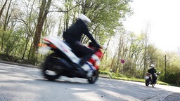 Zwei Motorradfahrer fahren auf einer Landstraße.