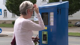 Eine Frau mit grauen Haaren steht vor einem Parkautomaten