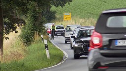 Ein Fahrradfahrer fährt mit Autofahrern zusammen auf einer Bundesstraße.