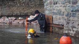 Zwei Männer in Tauchausrüstung arbeiten im Wasser am Fuß eines Brückenpfeilers.