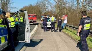 Eine Person sowie Polizeibeamte mit Fahrzeugen auf einer Straße 