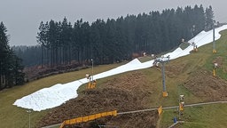 Auf dem Foto ist Skihang zu sehen, auf dem nur ein schmaler Streifen mit Schnee bedeckt ist