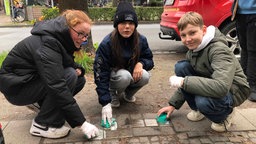 Die Schüler*innen machen die Metallmarkierung auf dem Boden sauber.