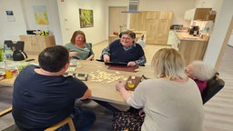 Bewohner des Tageshospiz sitzen an einem Tisch unnd spielen Rummikub