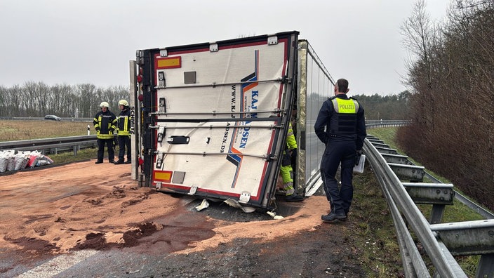 ein umgekippter LKW, davor und dahinter Polizisten und Feuerwehrleute