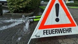 Wasser fließt aus dem Schlauch und davor steht ein Schld "Feuerwehr"