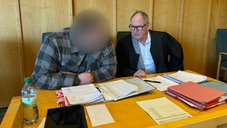 Der Täter sitzt mit seinem Verteidiger im Gerichtssaal. Sein Gesicht ist nicht zu erkennen.