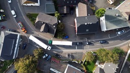 Luftaufnahme einer schmalen Straße im Wohngebiet, auf der 2 LKW aneinader vorbeifahren.