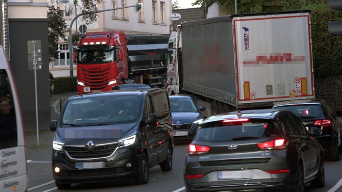 Zwei LKW versuchen auf einer engen Straße aneinander vorbei zu fahren. Es entsteht ein Stau. 