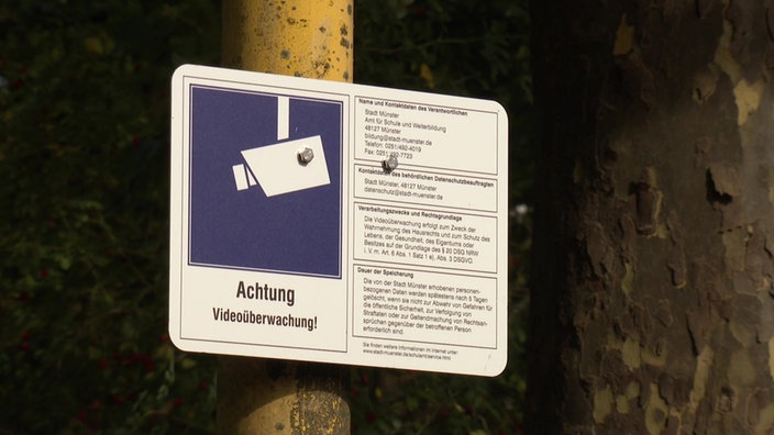 Auf dem Bild sit ein Schild mit einem Kamera-Piktogramm zu sehen. Es weist daraufhin, dass an dieser Stelle Aufnahmen von einer Kameraüberwachung gemacht werden.