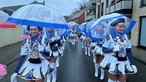 Eine Gruppe Frauen in weißen Kostümen mit blauen Regenschirmen