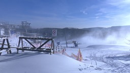 Eine Schneekanone steht auf einer verschneiten Piste