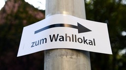 Ein Papierschild ist an einem Laternenmast befestigt, daruaf steht "Zum Wahllokal" und ein Pfeil nach rechts.