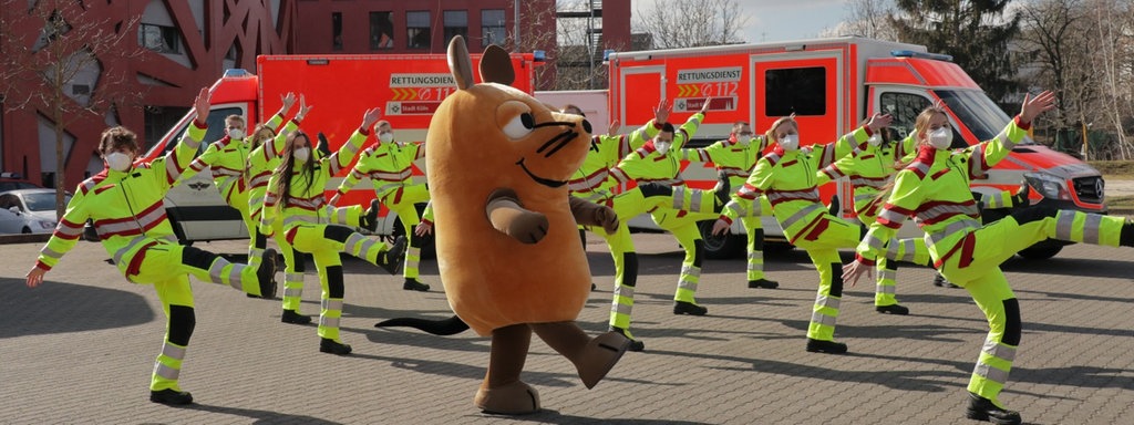 Die Maus tanzt gemeinsam mit Rettungssanitäterinnen und Rettungssanitätern