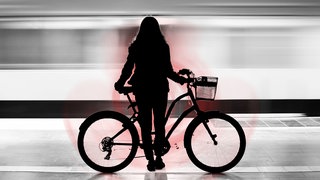 Eine Frau steht mit ihrem Fahrrad an einer U-Bahn-Haltestelle.