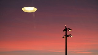 Ein roter Himmel, in dem sich eine Lampe spiegelt, die die Illusion eines Ufos ergibt.