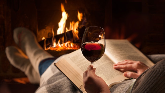 Frau am Kamin mit einem Buch und Rotwein