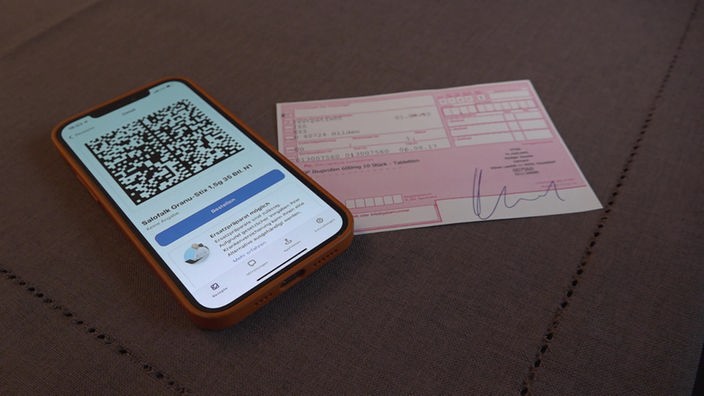 Ein Smartphone mit einem e-Rezept liegt neben einem klassischen Rezept