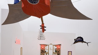 Fluxus and Beyond: Werk von Benjamin Patterson in der Ausstellung. Eine Gitarre mit Flügeln hängt von der Ecke. Vor Kopf ein Spiegeltisch. Rechts davon ein Fisch. 