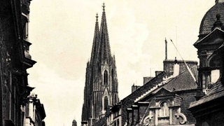 Ein altes schwarz-weiß Bild einer Kölner Straße mit Dom im Hintergrund.