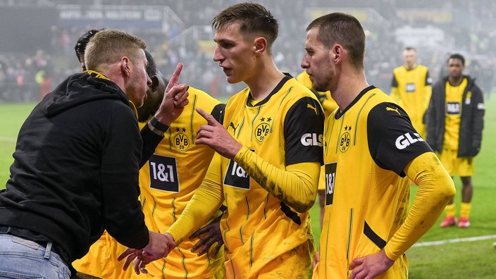 Dortmunder Spieler (mittig) um Nico Schlotterbeck, Waldemar Anton u.a. im Streitgespräch mit einem Fan (links) am Spielfeldrand, weitere BVB-Spieler im Hintergrund