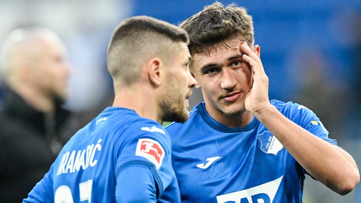 Spielszene: Hoffenheims Andrej Kramaric (mitte-links) und Hoffenheims Tom Bischof (r., mit Hand im Gesicht) stehen nachdenklich auf dem Platz, im Hintergrund (links unscharf) eine weitere Person