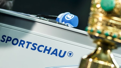 Mikrofon mit ARD-Logo über Sportschau-Schriftzug - im Vordergrund: unscharf fotografierter DFB-Pokal