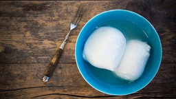 Zwei Kugeln Mozzarella mit etwas Flüssigkeit in einer Schale auf einem Holzbrett