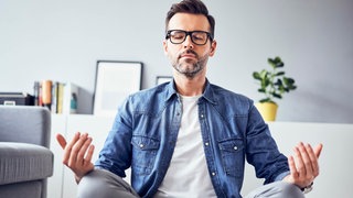 Ein Mann sitzt mit geschlossenen Augen in einer meditativen Haltung