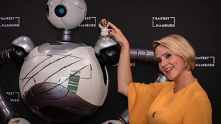 Judith Rakers setzt auf dem Filmfest Hamburg dem Roboter Rozzum aus dem Film "Der wilde Roboter" das Modell eines Gänsekükens auf die Schulter