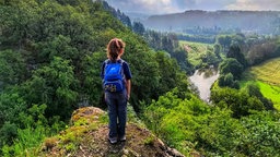 Ein Mädchen mit Rücksack steht auf einem Felsen und blickt über die hügelige Landschaft