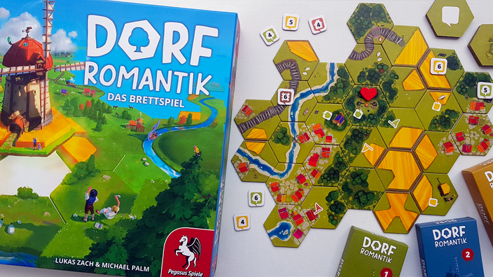 Die Schachtel von Dorfromantik neben einer Landschaft aus sechseckigen Spielplättchen, die Dörfer, Felder und Wälder zeigt