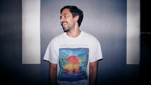 Max Giesinger posiert lächelnd vor einer Wand für die Kamera