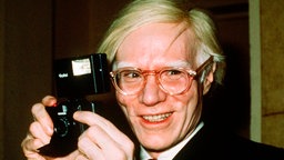 Andy Warhol lächelt an der Kamera vorbei.