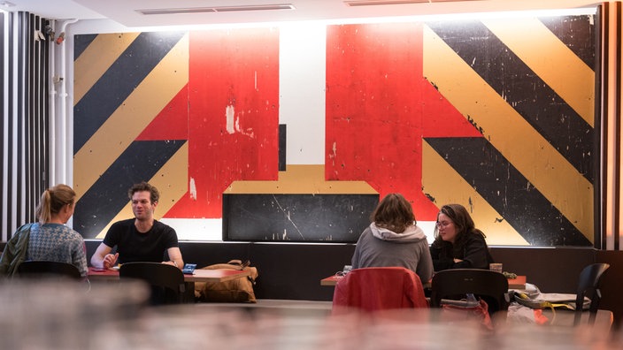 Mitarbeiter und Mitarbeiterinnen des Theaters sitzen vor einem Presserundgangs im Berliner Ensemble für das Kunstwerk «Berliner Assemblage» in der Kantine, an deren Wand die Kunstwerke hängen.