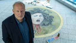 Szene aus dem Tatort: Der Schauspieler Axel Milberg schaut in die Kamera. Am Boden ist eine mit Kreide gemalte Medusa.