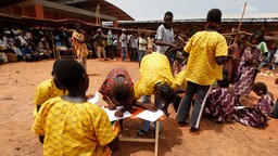 Das Operndorf Afrika zeigt Kinder in Burkina Faso, die schreiben. Im Hintergund sind Menschen versammelt. 