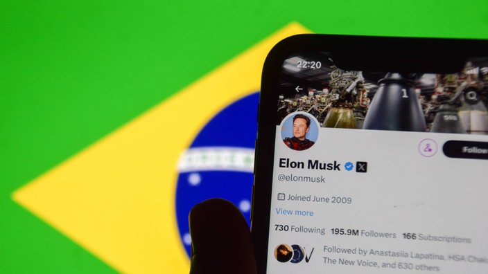 Das X-Profil von Elon Musk auf einem Handy mit der Brasilianischen Flagge im Hintergrund.