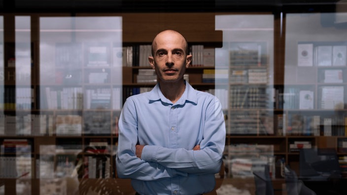 Yuval Noah Harari mit verschränkten Armen vor der Glasfront seines Büros.