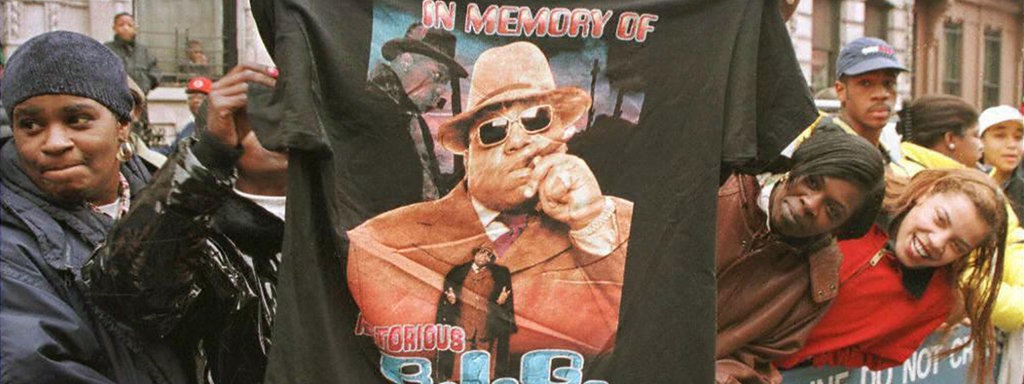 Fans entlang einer Absperrung; Ein Mann hält ein T-Shirt mit der Aufschrift "In memory of Notorius B.I.G." und dessen Gesischt hoch.