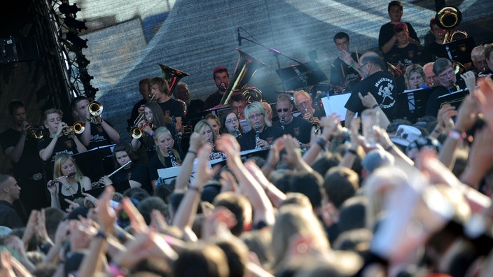 Wacken Festival: Zuschauer:innen vor einer Bühne, auf der eine Kapelle spielt.