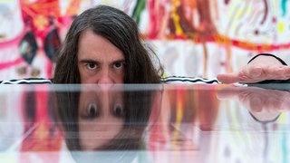 Jonathan Meese, Maler und Aktionskünstler, spiegelt sich in dem Ausstellungsraum der Ausstellung "Die Irrfahrten des Meese" in einem Schaukasten.