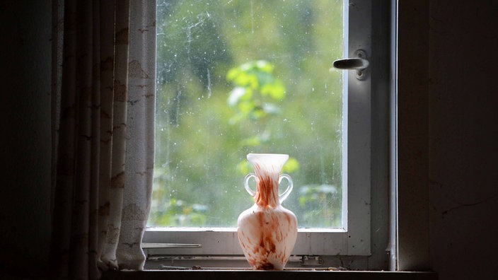 Eine Vase steht in einem verlassenen Haus auf der Fensterbank.