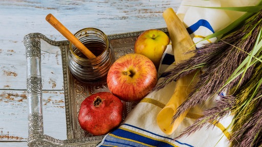 Äpfel und Granatenäpfel liegen neben einem Honigtopf und einem Schofarhorn auf einem Tisch