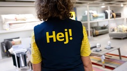 Eine Mitarbeiterin von IKEA, auf deren Weste in großen Buchstaben "Hej!" steht, in der Ausstellungsfläche einer Filiale in Eching bei München. 