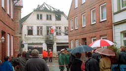 Das Archivbild vom 23.11.1992 zeigt Schaulustige und Feuerwehrleute vor dem Haus in der Möllner Mühlenstraße, auf das in der Nacht ein rassistisch motivierter Brandanschlag verübt worden war.