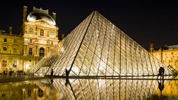 Blick auf das Pariser Kunstmseum Le Louvre mit der hell erleuchteten Pyramide am Abend.