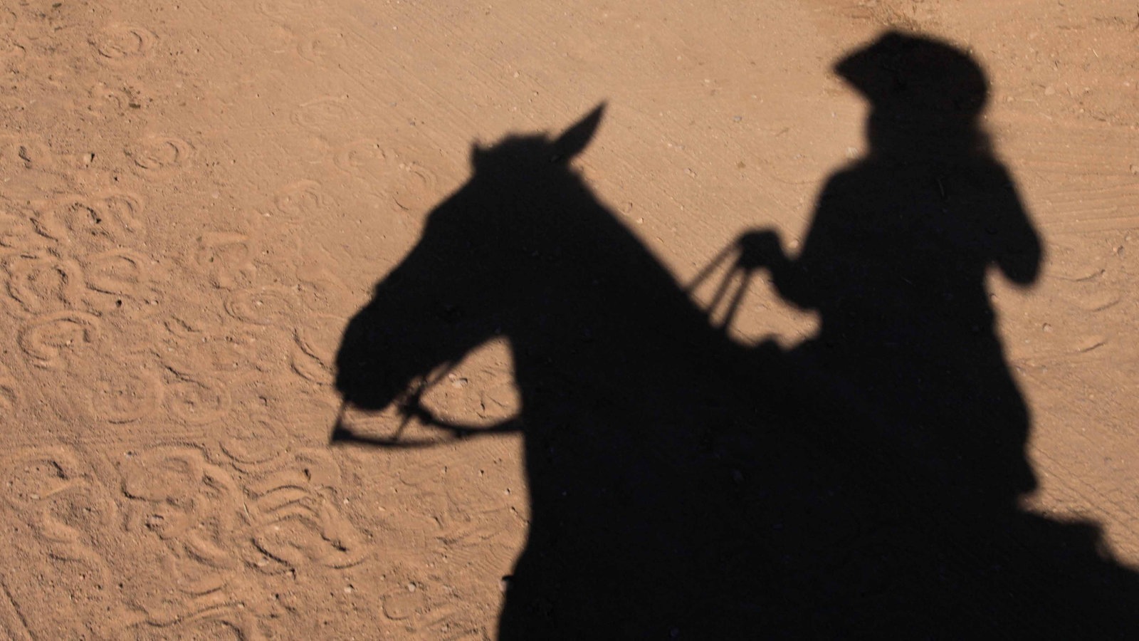 Ein Cowboy reitet auf seinem Pferd, zu sehen ist nur sein Schatten.