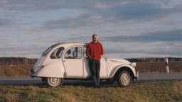 Ein junger Mann steht vor einem Citroen 2CV6 bei Deining, südlich von München.