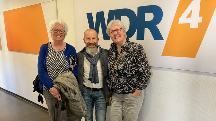 Die Buchclub-Mitglieder Dirk Klauke, Ruth Lobach und Susanne Ludwig stehen vor dem WDR 4-Logo